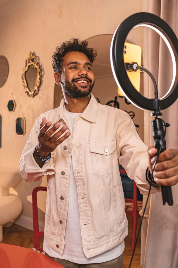 Smiling vlogger using a ring light in a cozy indoor setting.